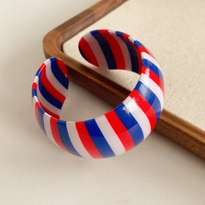 Detail of red white and blue striped resin cuff bracelet on a linen display board