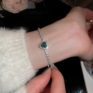 Macro detail of silver heart bracelet with emerald green stone and zircon stones