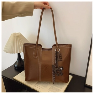 Detail of brown tote bag with white contrast stitching and cute cat leather pendant