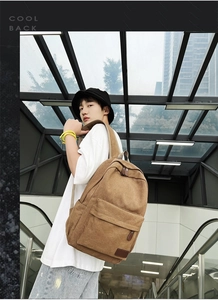 Side view of a large brown canvas backpack with leather details worn by a model in the city