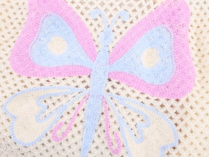 Macro detail of hand-crocheted fabric featuring pink and blue butterfly embroidery pattern