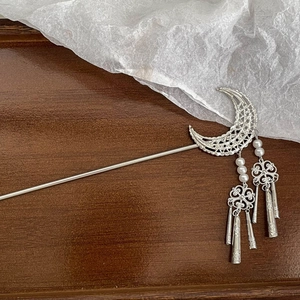 Detailed close-up of a silver metal hair pin with moon crescent and tassel details