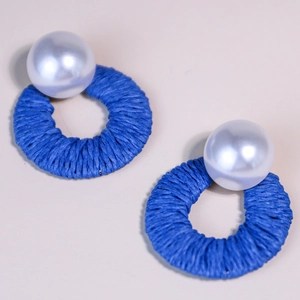 Detailed macro view of royal blue raffia woven circular earrings with white pearl accents