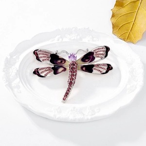 Detailed close-up of dragonfly brooch with purple enamel wings on white porcelain plate