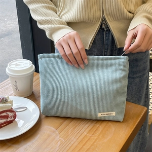 Close-up of a light blue corduroy cosmetic pouch held by hands in a cozy cafe setting