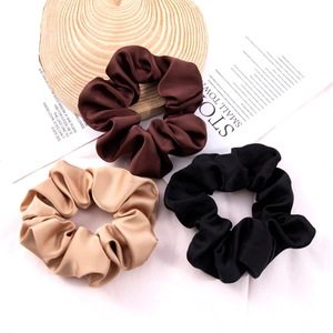 Three silk satin hair scrunchies in dark brown, black, and champagne gold on wood decor