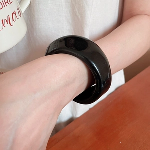 Close-up of a wide black acrylic bangle with a polished resin finish on a woman's wrist
