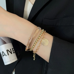 Dettaglio di un set di tre braccialetti dorati con maglia a serpente e ciondolo al polso