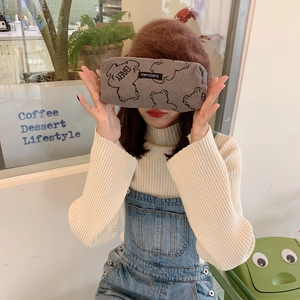 Brown corduroy pencil case with bear print held by a person in a cozy cafe setting