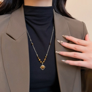 Detail of vintage tiger eye flower pendant necklace worn over a black turtleneck top