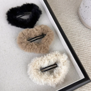 Three plush heart hair clips in black, brown, and cream on a soft fabric tray