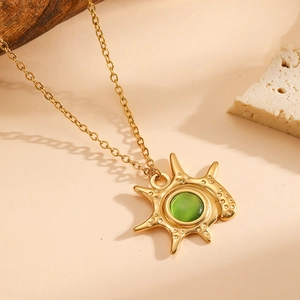 Vintage 18K gold plated sunburst necklace featuring a central green gemstone on stone background