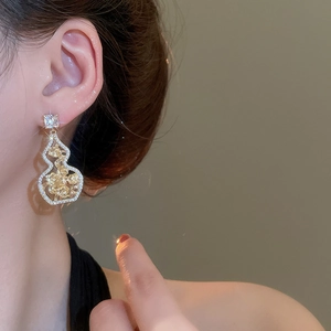 Close-up of golden hollow gourd earrings with rose flower inlay and zircon stones