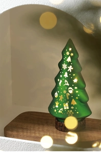 Close-up of a lit green frosted Christmas tree lamp with festive patterns on a wood base