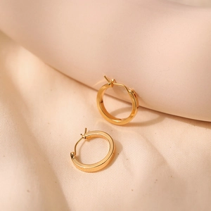 Detailed view of polished 18K gold plated minimalist hoop earrings on beige fabric