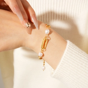 Close-up of gold chain link bracelet with freshwater pearls worn over a white knit sleeve