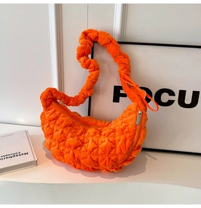 Detailed close-up of bright orange quilted dumpling bag with soft ruched strap and texture