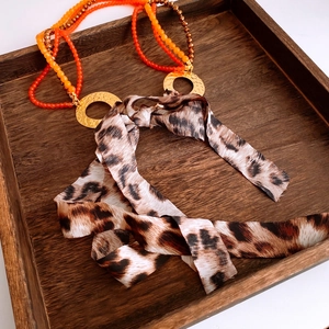 Detail of layered orange beads with leopard print fabric ribbon on wooden tray