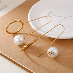 Elegant gold geometric earrings with pearls on a ceramic dish and notebook