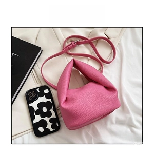 Detail view of the rose pink lychee leather texture and curved handle on the crossbody bag