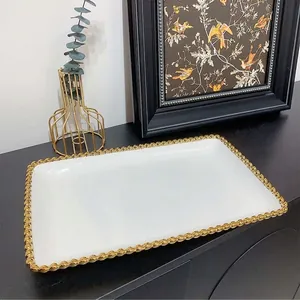Macro shot of white ceramic tray with gold beaded edge on dark tabletop surface