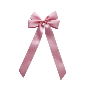 Detail of pink satin bow hair clip with long ribbon tails and glossy fabric texture