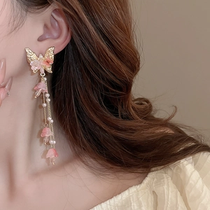 Détail de boucles d'oreilles à franges avec papillon doré, fleurs roses et perles blanches
