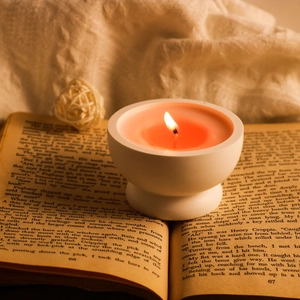Portacandela minimalista in ceramica bianca su un libro d'epoca con una calda luce arancio