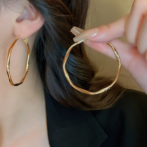 Detail of gold large twisted hoop earrings with hammered texture and vintage finish