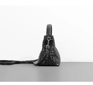 Side view of black woven leather handbag with handles and detachable shoulder strap