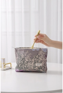Close-up of floral jacquard makeup bag with gold beauty tool being placed inside