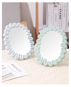 Detail of light blue and mint green wavy frame oval mirrors on a soft beige knit fabric