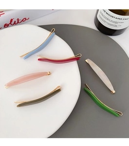 Close-up of colorful acetate hair clips with gold metal base on a white ceramic plate