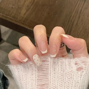 Detailed view of French-style press-on nails with white tips and delicate polka dots
