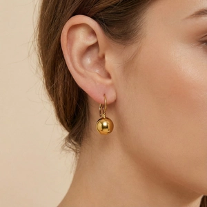 Detailed close-up of a high-polished golden ball earring worn by a model in profile