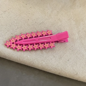 Pince à cheveux rose avec étoiles jaunes et clip bec de canard sur fond beige