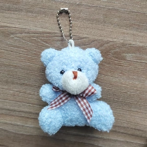 Close-up of blue curly plush bear keychain with checkered bow on wooden background