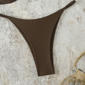 Close-up of chocolate brown high-cut bikini bottoms with side straps on stone surface