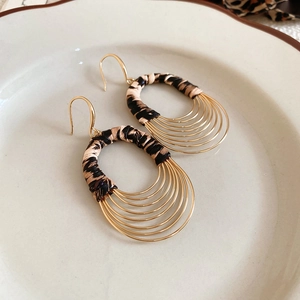 Macro view of leopard print texture and golden multi-layered oval earrings in a ceramic dish
