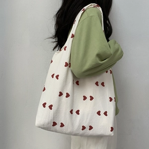 Side view of white canvas tote bag with red heart patterns worn on shoulder