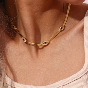 Close-up of gold evil eye necklace with crystals on flat snake chain on neck
