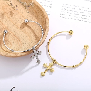 Detailed shot of gold and silver rose cross charms on stainless steel open bangles