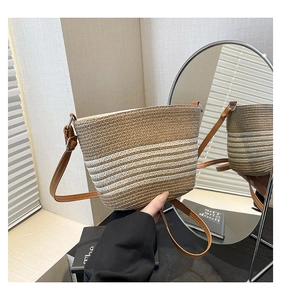 Detail of hand-woven straw bucket bag with brown stripes and leather shoulder strap