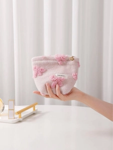 Sweet pink plush makeup bag with floral bow and gold zipper detail held by hand