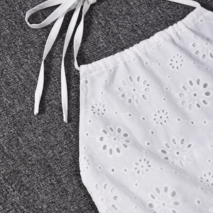 Close-up of white floral embroidery and lace-up detail on a hollow-out crop top
