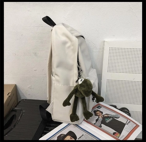 Détail d'un sac à dos blanc cassé avec un accessoire de grenouille en peluche verte