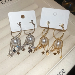 Macro view of C-shape pearl earrings with zircon star tassels in silver and gold finish