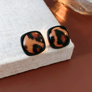 Detail of square acrylic earrings with leopard print and black frame on beige texture