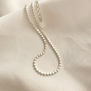Minimalist S925 sterling silver anklet with flat beads and oval tag on fabric background