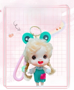 Detailed view of cartoon doll keychain with golden pigtails and green dress on pink grid